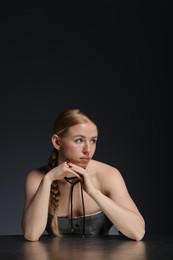 Photo of Beautiful woman with pigtail posing at table on dark background