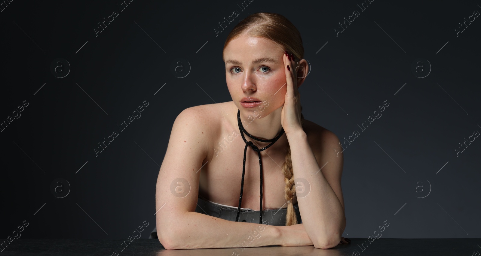 Photo of Fashionable portrait of beautiful woman with pigtail posing at table on dark background