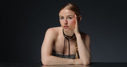 Photo of Fashionable portrait of beautiful woman with pigtail posing at table on dark background
