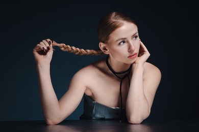 Photo of Beautiful woman with pigtail posing at table on dark background