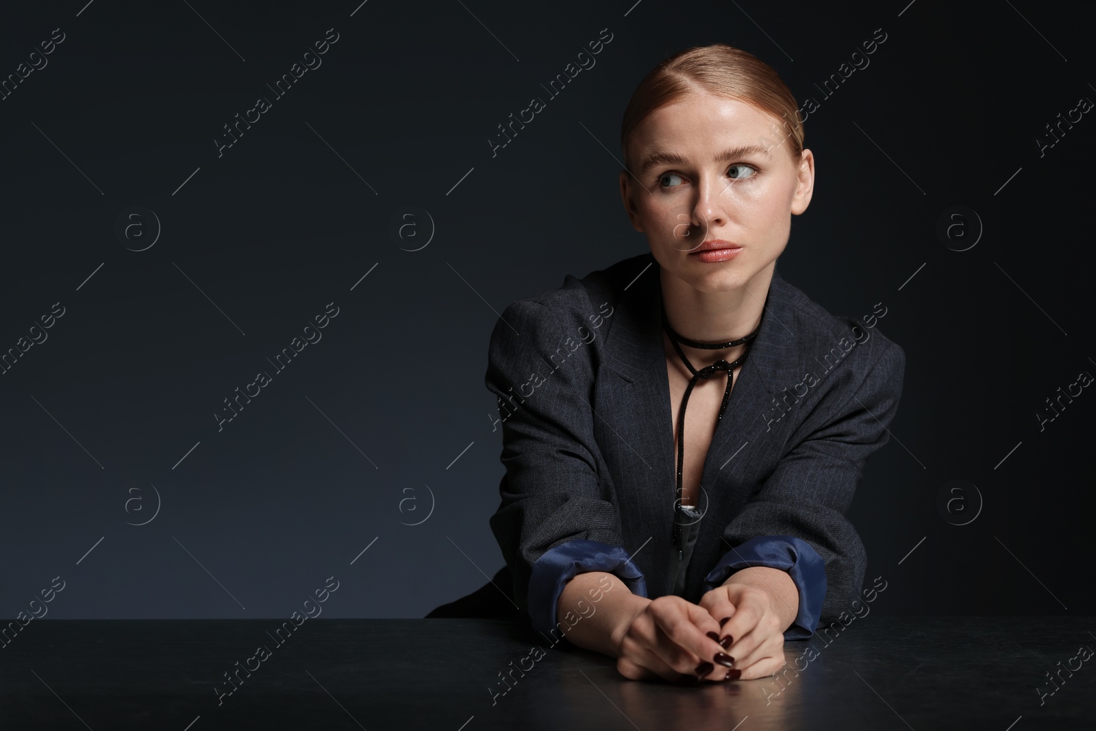 Photo of Beautiful woman with pigtail in suit posing at table on dark background. Space for text