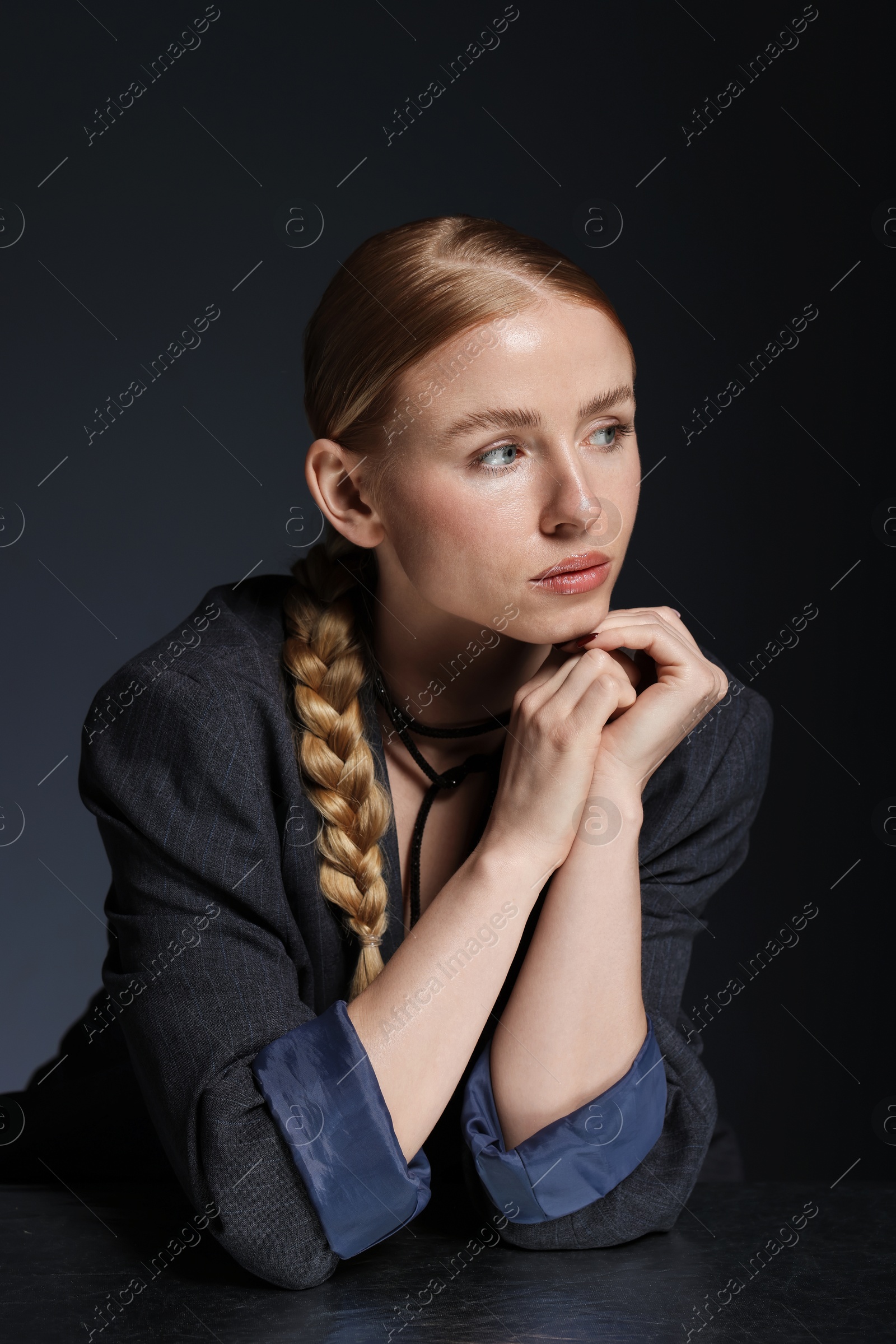 Photo of Beautiful woman with pigtail in suit posing at table on dark background