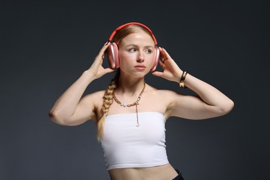 Photo of Beautiful woman in stylish bijouterie, headphones and top posing on dark grey background