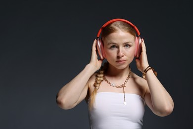 Photo of Beautiful woman in stylish bijouterie and headphones on dark grey background. Space for text