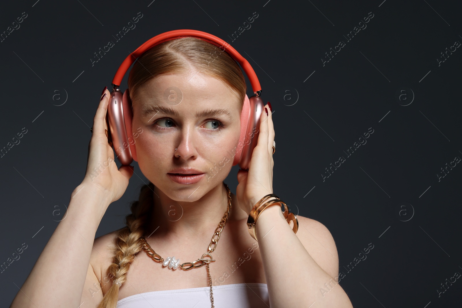 Photo of Beautiful woman in stylish bijouterie and headphones on dark grey background