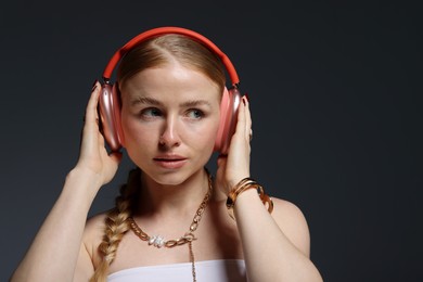Photo of Beautiful woman in stylish bijouterie and headphones on dark grey background