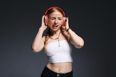 Photo of Playful woman in stylish bijouterie, headphones and top posing on dark grey background