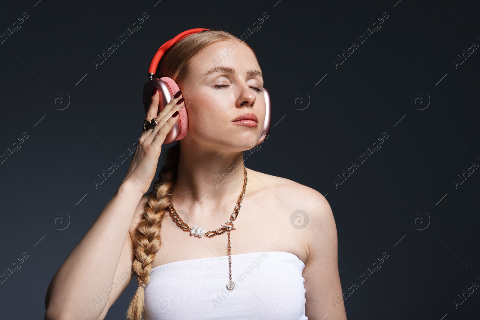 Photo of Beautiful woman in stylish necklace and headphones posing on dark grey background