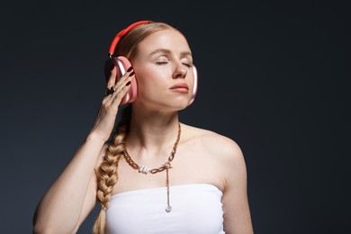 Photo of Beautiful woman in stylish necklace and headphones posing on dark grey background