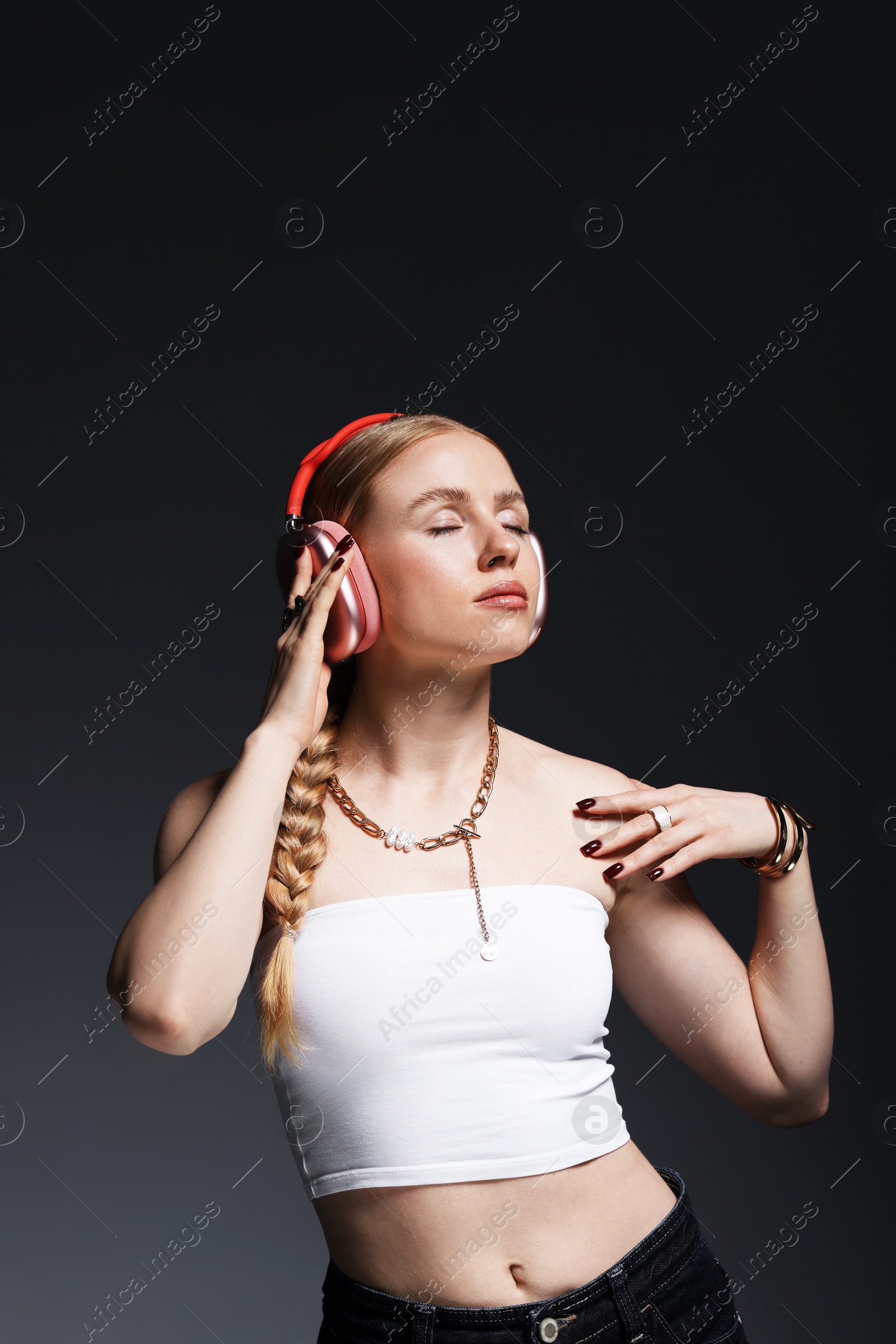 Photo of Beautiful woman in stylish bijouterie, headphones and top posing on dark grey background
