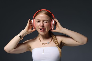 Photo of Playful woman in stylish bijouterie, headphones and top posing on dark grey background