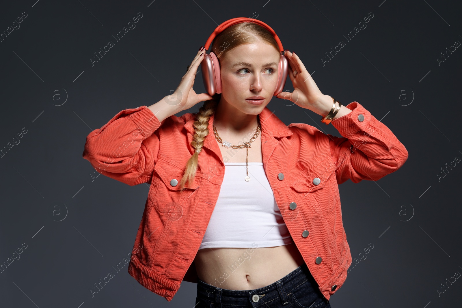 Photo of Beautiful woman in stylish bijouterie, headphones and jacket posing on dark grey background
