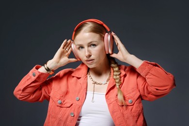 Photo of Fashionable portrait of beautiful woman in stylish bijouterie, headphones and jacket on dark grey background