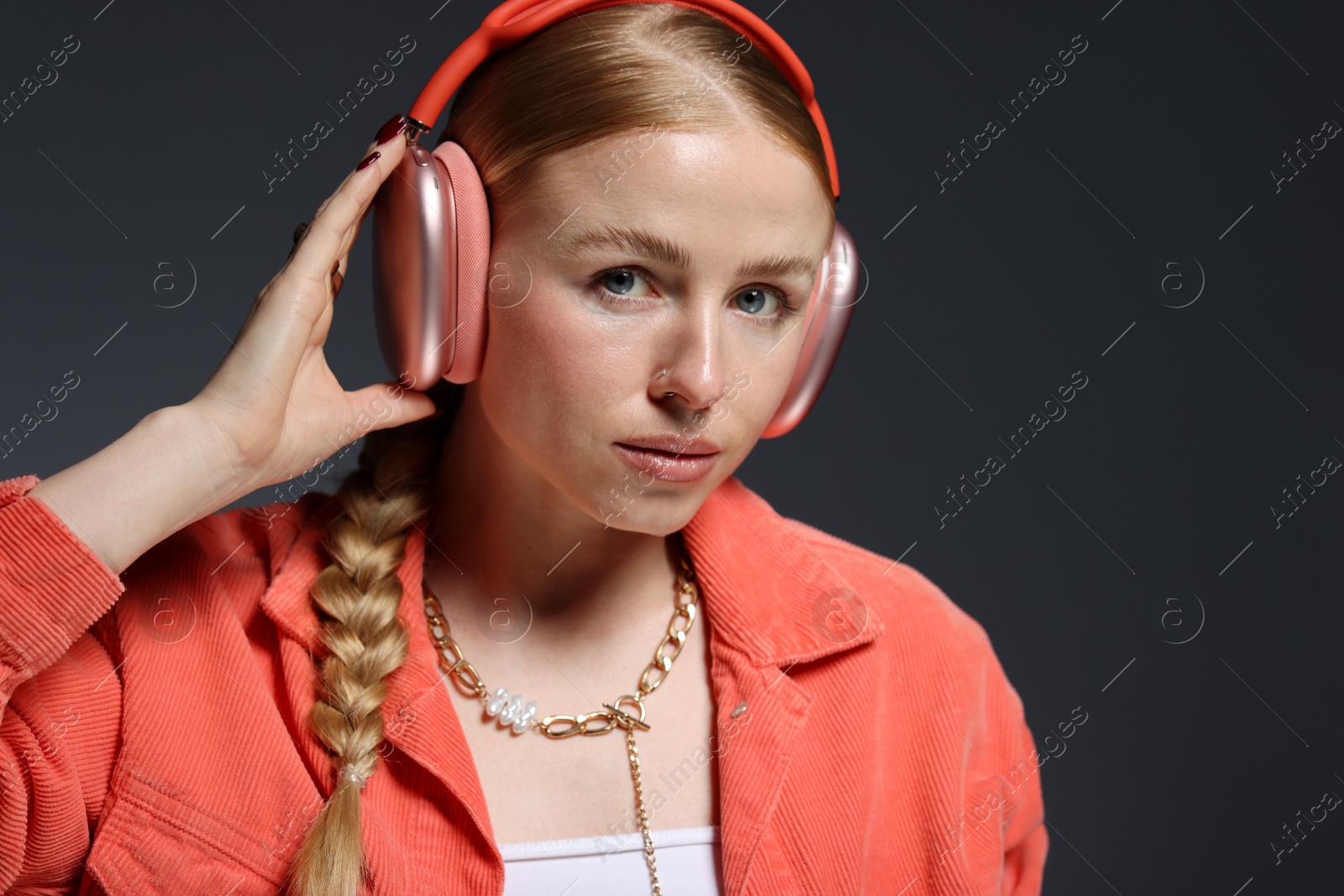 Photo of Fashionable portrait of beautiful woman in stylish necklace, headphones and jacket on dark grey background