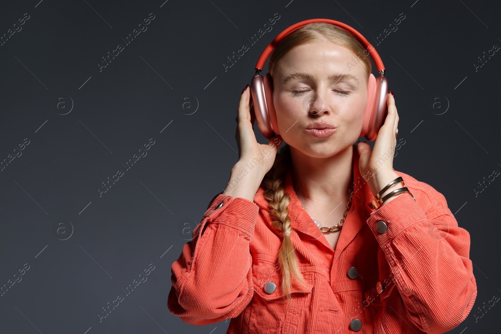 Photo of Beautiful woman in stylish bijouterie, headphones and jacket on dark grey background. Space for text