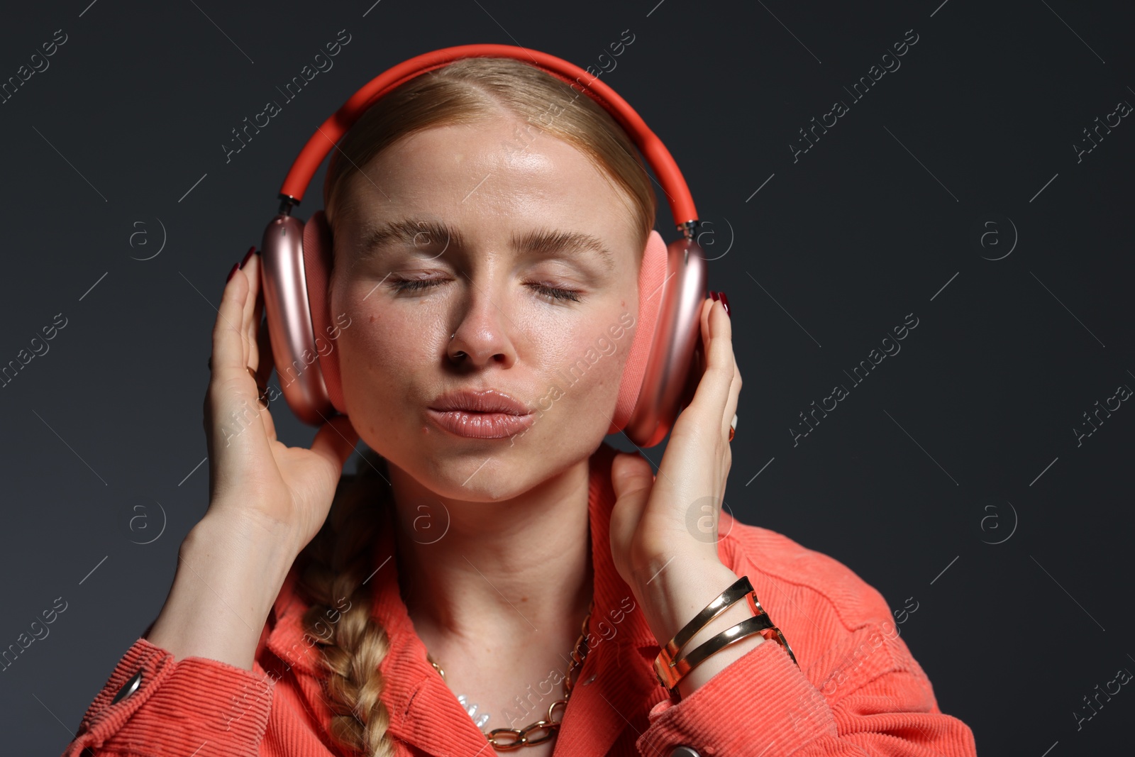 Photo of Beautiful woman in stylish bijouterie, headphones and jacket on dark grey background