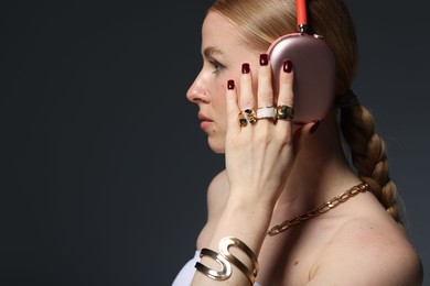 Photo of Beautiful woman in stylish bijouterie and headphones listening to music on dark grey background. Space for text