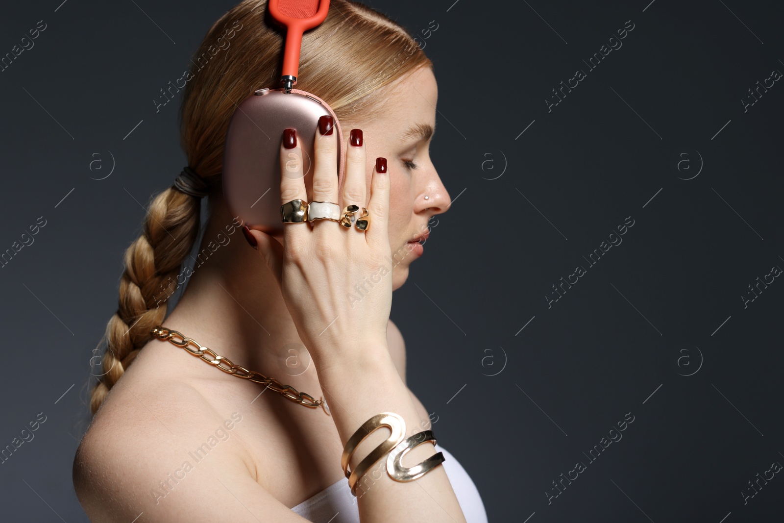 Photo of Beautiful woman in stylish bijouterie and headphones listening to music on dark grey background. Space for text