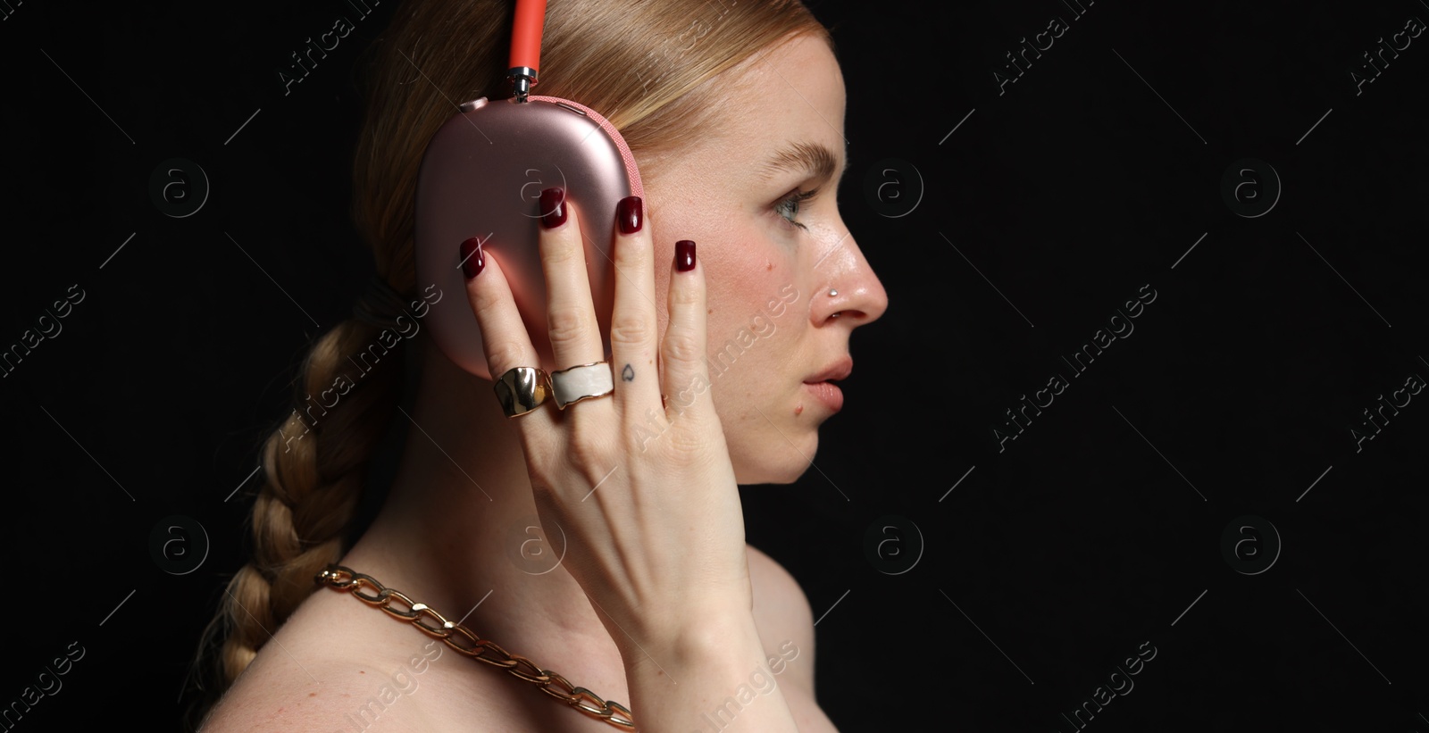 Photo of Beautiful woman in stylish bijouterie and headphones listening to music on black background, closeup. Space for text