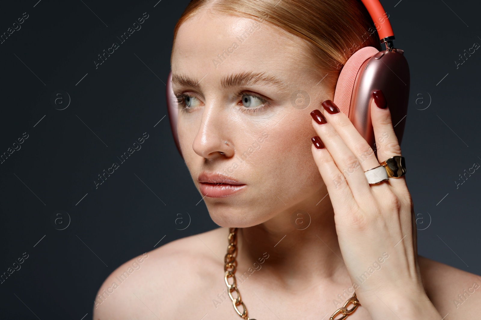 Photo of Beautiful woman in stylish bijouterie and headphones listening to music on dark grey background, closeup