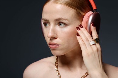 Photo of Beautiful woman in stylish bijouterie and headphones listening to music on dark grey background, closeup