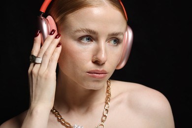 Photo of Beautiful woman in stylish bijouterie and headphones listening to music on black background, closeup