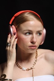 Photo of Beautiful woman in stylish bijouterie and headphones listening to music on black background, closeup