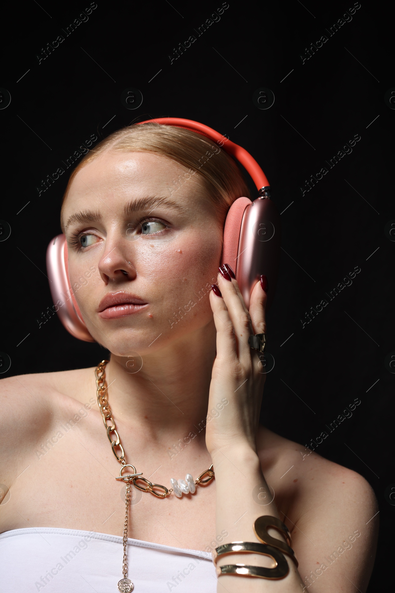 Photo of Beautiful woman in stylish bijouterie and headphones listening to music on black background, closeup