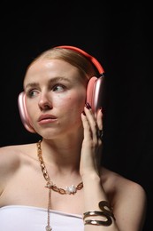 Photo of Beautiful woman in stylish bijouterie and headphones listening to music on black background, closeup