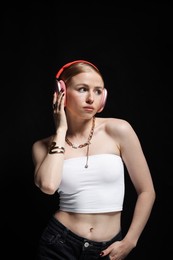 Photo of Beautiful woman in stylish bijouterie, top and headphones listening to music on black background