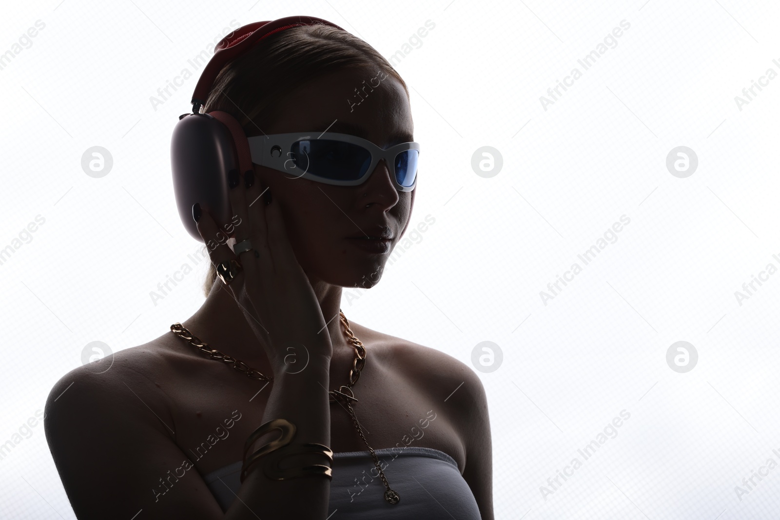 Photo of Beautiful woman in stylish sunglasses, bijouterie and headphones listening to music on white background