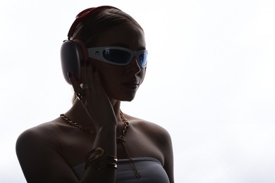Photo of Beautiful woman in stylish sunglasses, bijouterie and headphones listening to music on white background