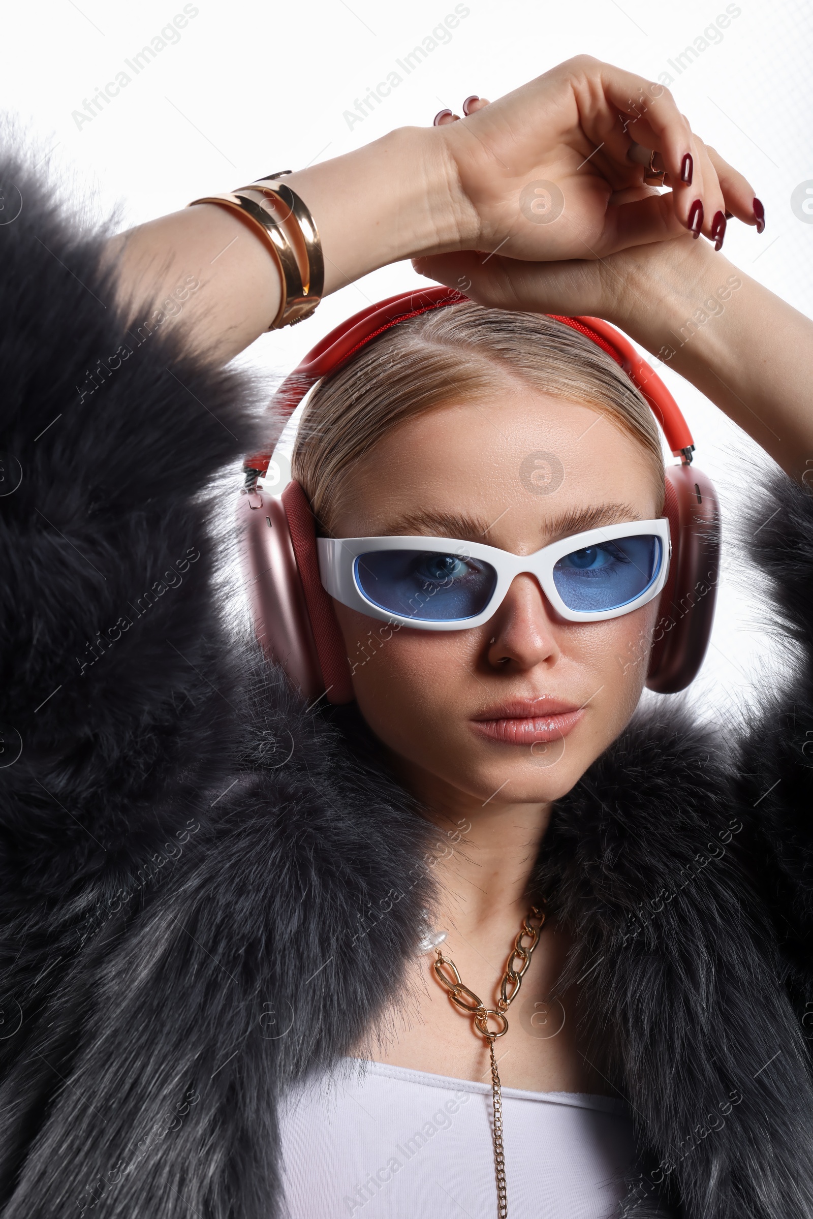 Photo of Fashionable portrait of beautiful woman in stylish sunglasses, bijouterie, fur coat and headphones listening to music on white background