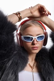 Photo of Fashionable portrait of beautiful woman in stylish sunglasses, bijouterie, fur coat and headphones listening to music on white background