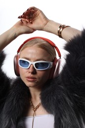 Photo of Beautiful woman in stylish sunglasses, bijouterie, fur coat and headphones listening to music on white background