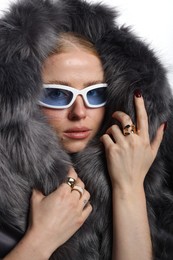 Photo of Fashionable portrait of beautiful woman in stylish sunglasses, rings and fur coat on white background