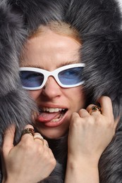 Photo of Fashionable portrait of playful woman in stylish sunglasses, rings and fur coat, closeup