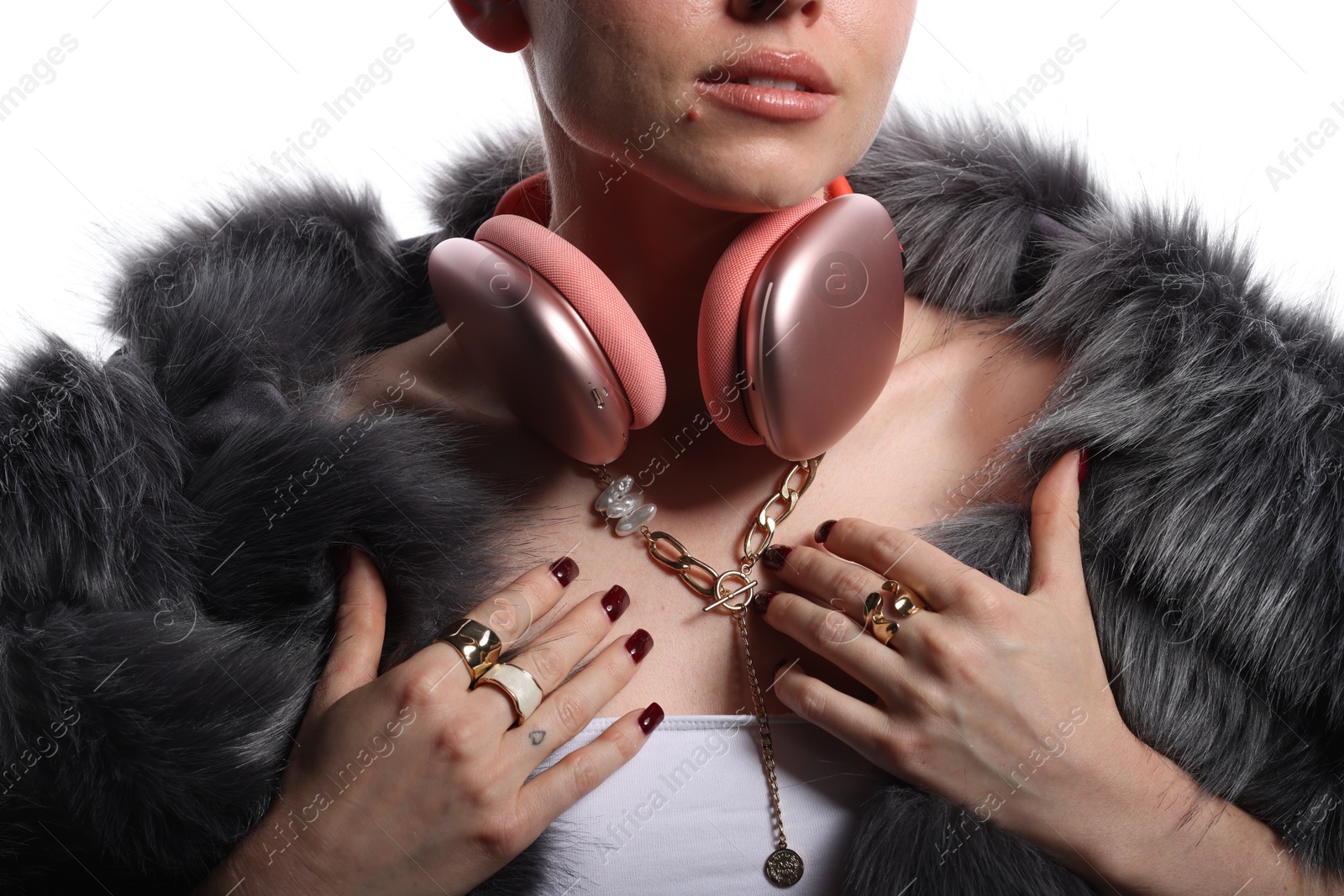 Photo of Woman in stylish bijouterie, fur coat and headphones on white background, closeup