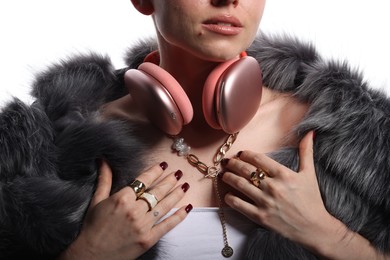 Photo of Woman in stylish bijouterie, fur coat and headphones on white background, closeup