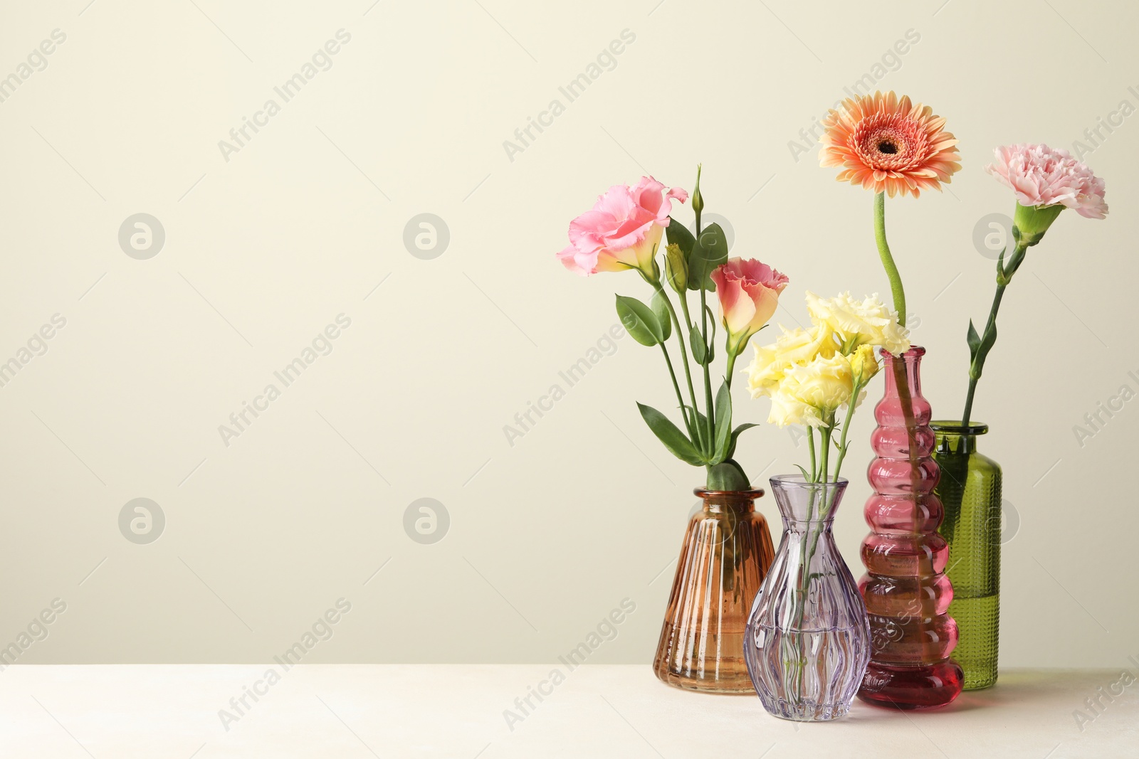 Different beautiful flowers in glass vases on white table against light grey background, space for text Photo of Different beautiful flowers in glass vases on white table against light grey background, space for text