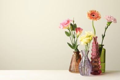 Photo of Different beautiful flowers in glass vases on white table against light grey background, space for text