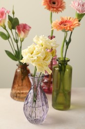 Photo of Different beautiful flowers in glass vases on white table against light grey background, closeup