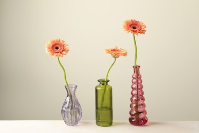 Photo of Beautiful gerbera flowers in glass vases on white table against light grey background