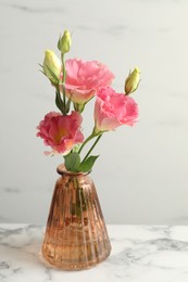 Photo of Beautiful eustoma flowers in glass vase on white marble table, closeup