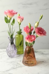 Photo of Beautiful eustoma flowers in glass vases on white marble table