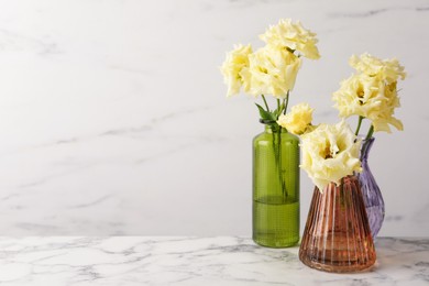 Photo of Beautiful eustoma flowers in glass vases on white marble table, space for text