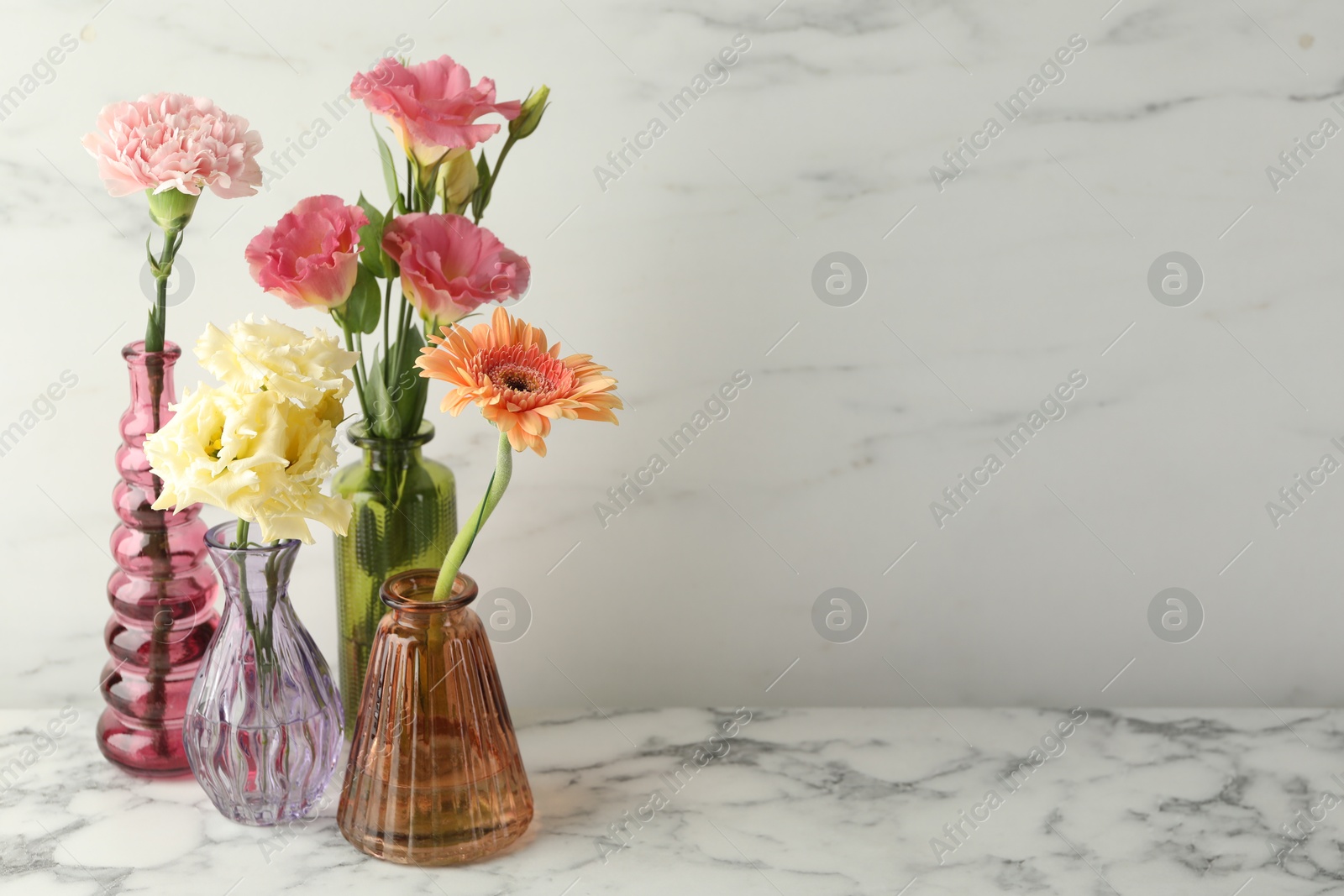 Photo of Different beautiful flowers in glass vases on white marble table, space for text