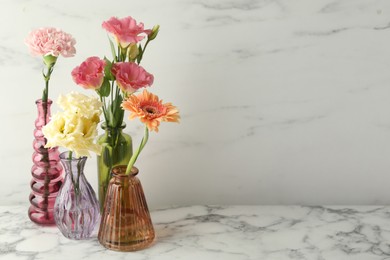 Photo of Different beautiful flowers in glass vases on white marble table, space for text