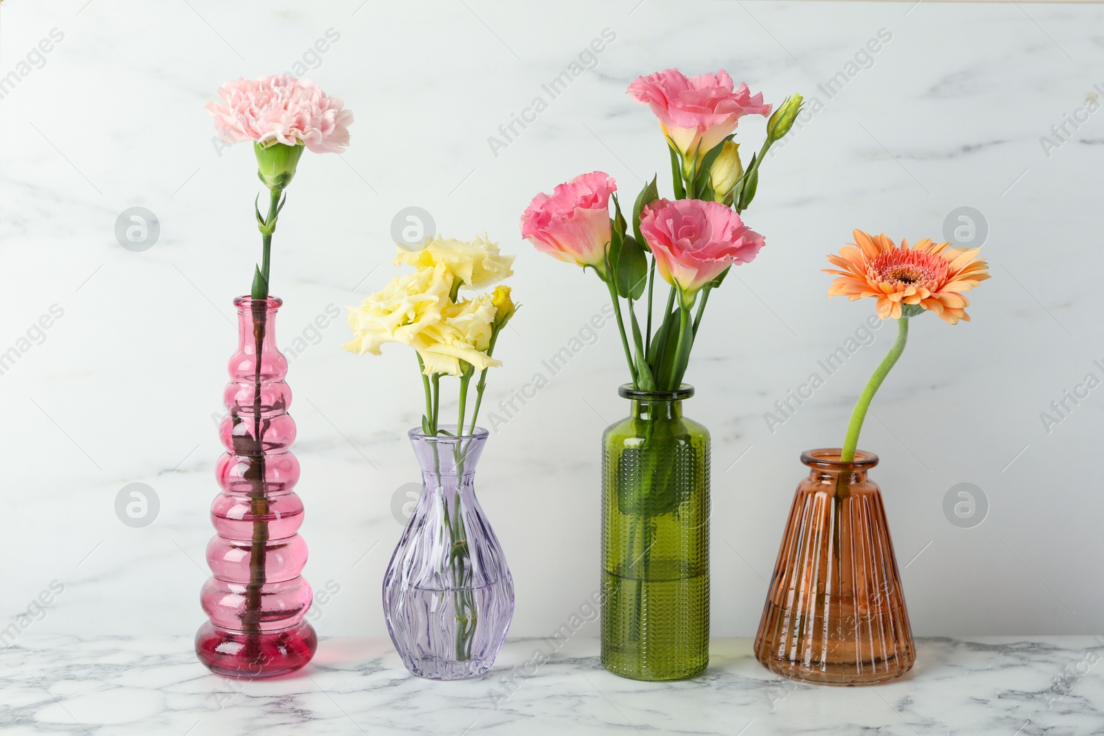 Different beautiful flowers in glass vases on white marble table Photo of Different beautiful flowers in glass vases on white marble table