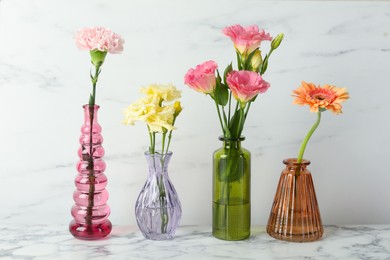 Photo of Different beautiful flowers in glass vases on white marble table
